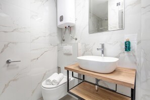 Et moderne badeværelse med et marmorgulv, en hvid vask på en træhylde, et toilet og en bruseniche med glasdør.