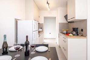 A modern kitchen with white cabinets, a dining table set for two, and a coffee machine. - City Seaview Apartment Vigo, Rijeka, Croatia (Rijeka)