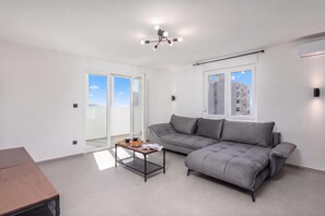 Un salon moderne avec un canapé gris, une table basse et une porte-fenêtre coulissante donnant sur un balcon.