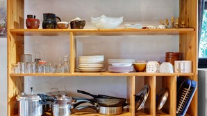 Una cocina con estantes de madera que contienen utensilios de cocina, incluyendo ollas, sartenes y platos.