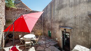 Un patio de piedra con una mesa, sillas y un paraguas rojo, además de una puerta.