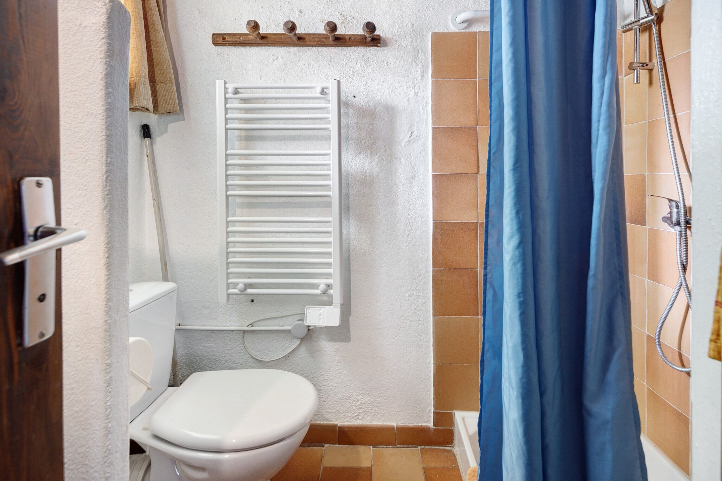 A bathroom with a toilet, a towel rack, a shower curtain, and a wall-mounted heater.