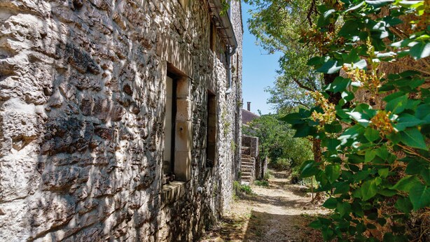 Un antiguo edificio de piedra con un estrecho sendero que lleva a una estructura de madera al fondo.