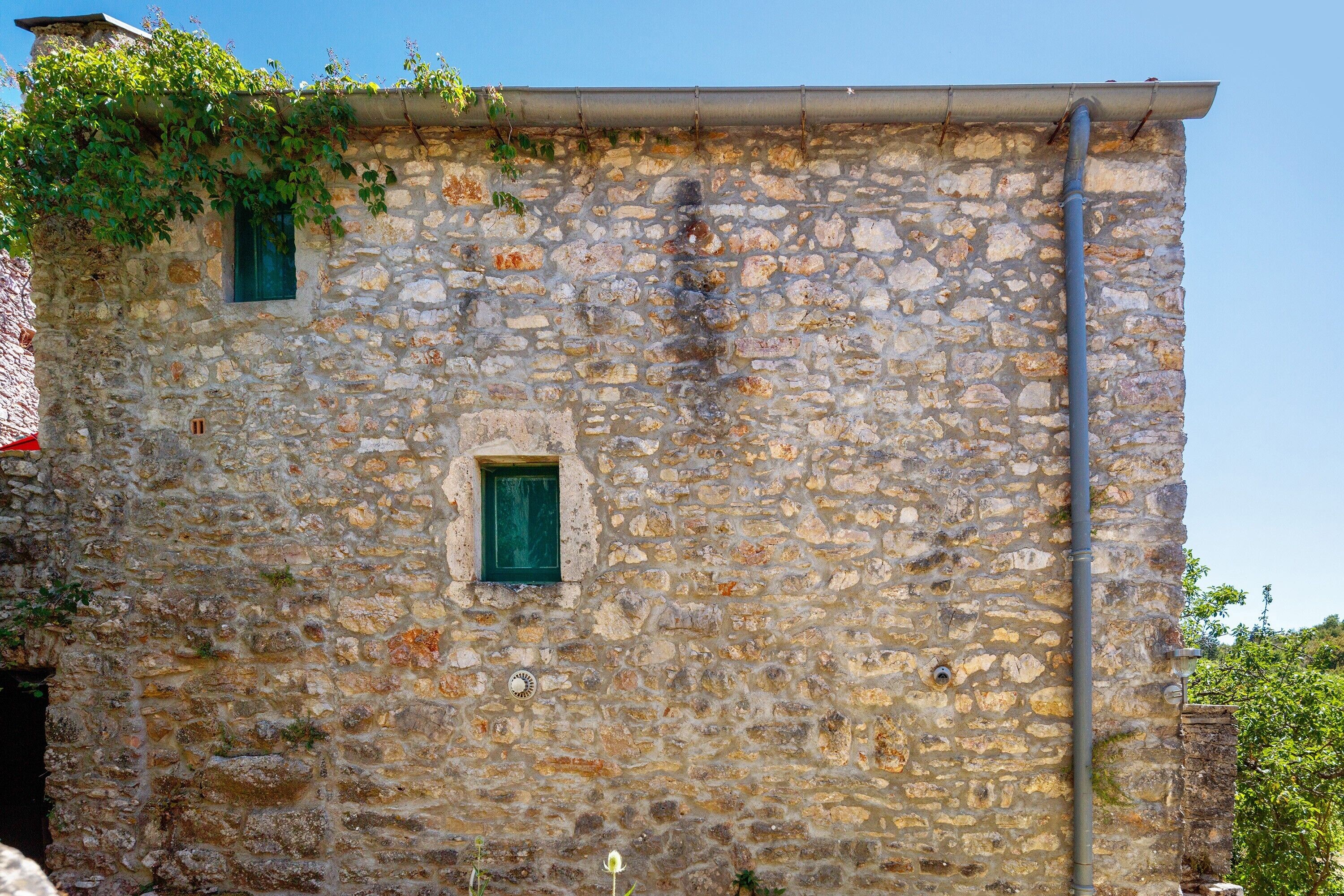 Um edifício de pedra com uma janela e uma porta pequena, rodeado por vegetação.