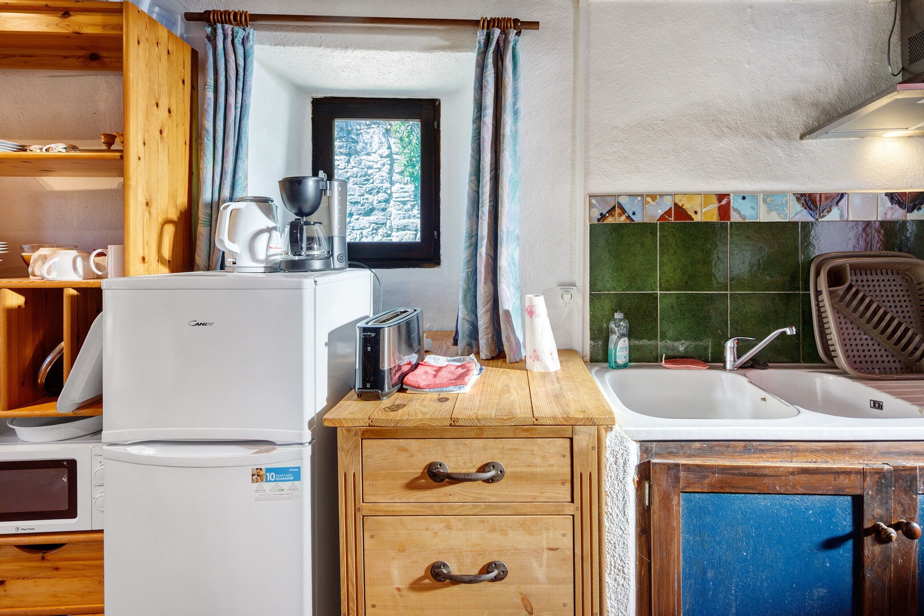 A compact kitchen with a refrigerator, toaster, coffee maker, and a wooden cabinet with drawers.