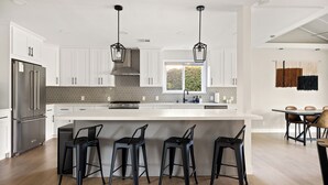 Une cuisine moderne avec des meubles blancs, un réfrigérateur en acier inoxydable, une cuisinière à gaz et un grand îlot central doté de tabourets de bar.