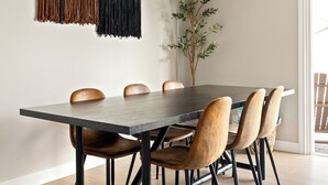 Un coin repas comprenant une longue table, six chaises, un ventilateur de plafond et une plante fixée au mur.