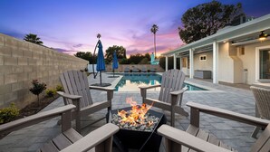 Un espace aménagé au bord de la piscine, avec des fauteuils Adirondack, un foyer et des parasols.