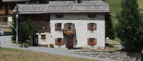 A traditional chalet with a stone facade, wooden shutters, and a balcony with flowers.