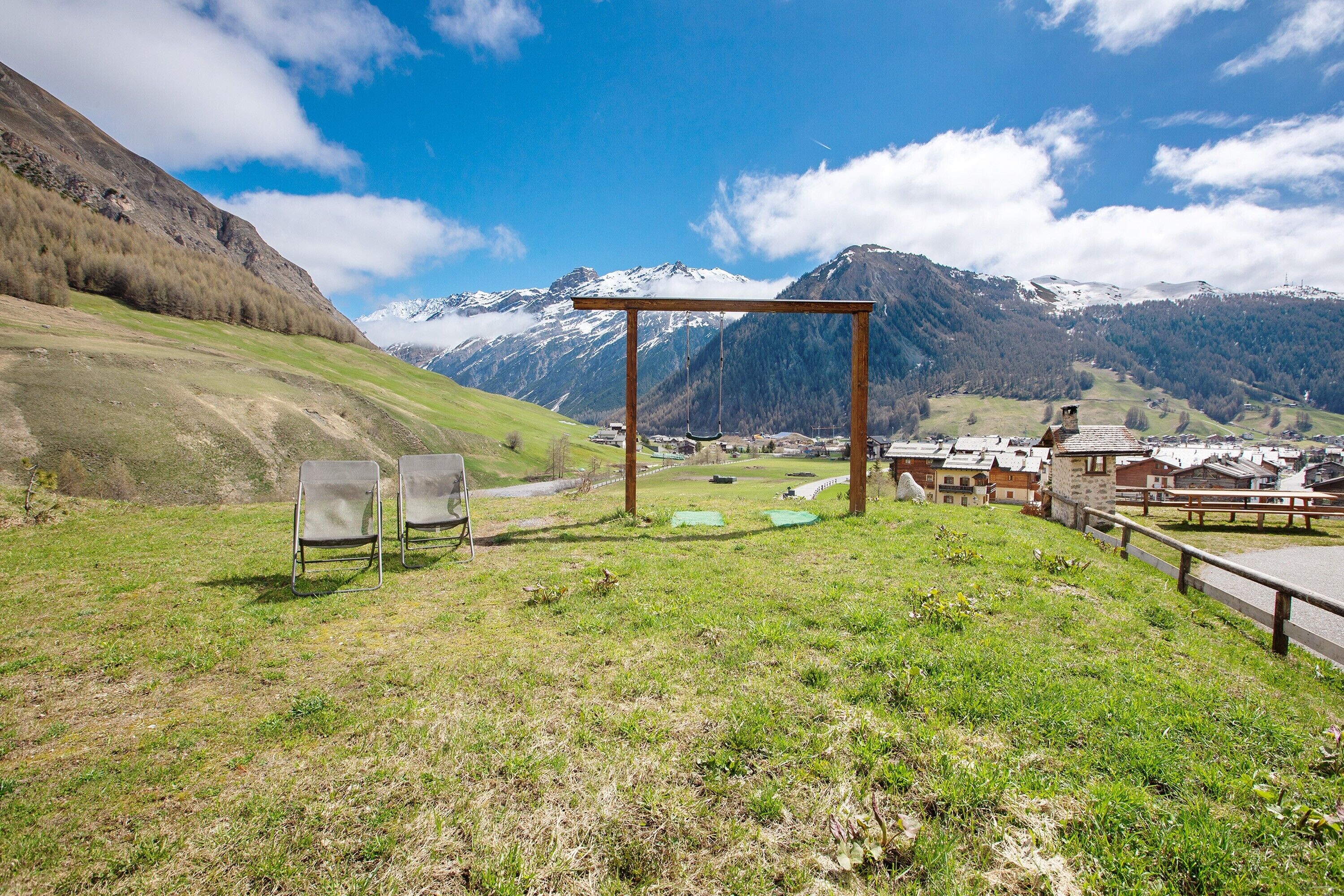 Un espace extérieur verdoyant, agrémenté d’une pergola en bois, de deux chaises et offrant une vue sur des montagnes enneigées.