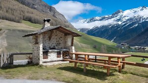A stone building with a wooden roof, a picnic table, and a view of snow-capped mountains. - Apartment 'La Lepre' with Lake View, Private Garden and Wi-Fi (Livigno)