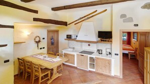 A rustic kitchen with wooden beams, a dining table with chairs, a microwave, and a coffee maker. - Apartment 'La Lepre' with Lake View, Private Garden and Wi-Fi (Livigno)