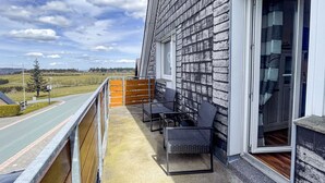 A balcony with outdoor furniture, a view of a road and fields, and a building with a brick exterior. - Fewo Renauweg - Gemütliche Ferienwohnung in Ruhiger Lage (Winterberg)