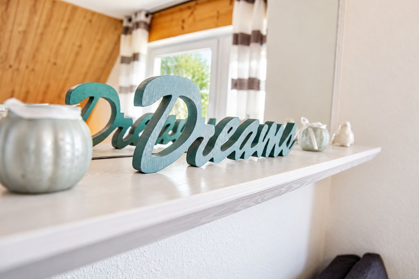 A white shelf with a decorative sign spelling 'Dream' and a small ceramic pot.