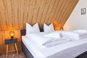 Une chambre avec un plafond en pente en bois, un lit avec du linge de lit blanc, deux lampes de chevet et une petite table de chevet avec une lampe.