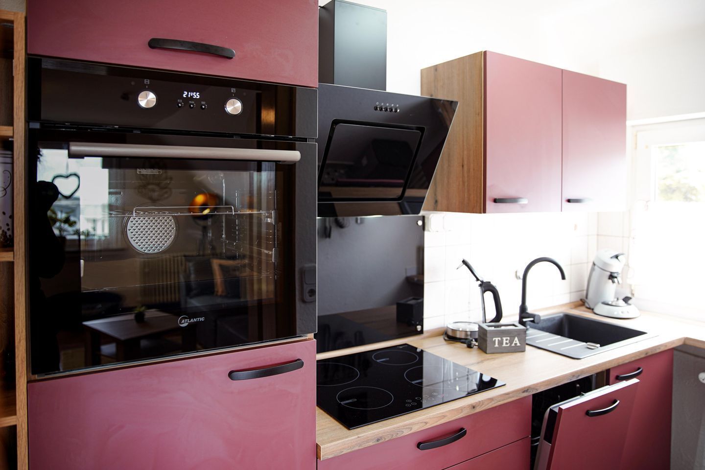 A modern kitchen with a built-in oven, a microwave, and a stove. There is a sink with a kettle and a tea infuser on the countertop.
