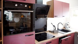 A modern kitchen with a built-in oven, a microwave, and a stove. There is a sink with a kettle and a tea infuser on the countertop. - Fewo Renauweg - Gemütliche Ferienwohnung in Ruhiger Lage (Winterberg)