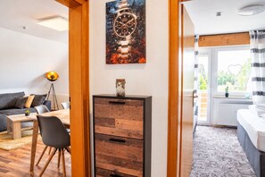 Un salon moderne avec un canapé, une table basse et une lampe. On y trouve un meuble en bois avec des tiroirs, et au-dessus, une œuvre d’art accrochée au mur.