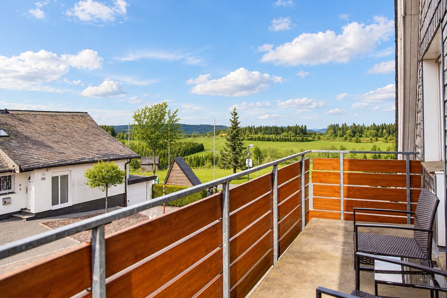 Een balkon met uitzicht op een groen landschap, een gebouw met huisnummer 35, en een houten hek.