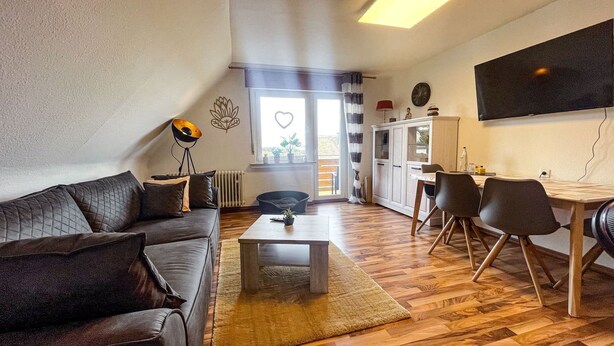 A modern living room with a sofa, coffee table, and dining area. - Fewo Renauweg - Gemütliche Ferienwohnung in Ruhiger Lage (Winterberg)
