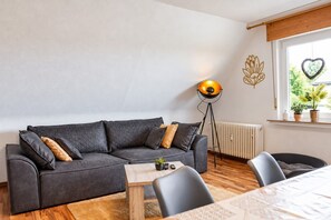 A modern living room with a dark grey sectional sofa, a wooden coffee table, and a floor lamp. - Fewo Renauweg - Gemütliche Ferienwohnung in Ruhiger Lage (Winterberg)