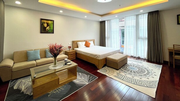 A modern hotel room with a bed, sofa, coffee table, and a large window with curtains.
