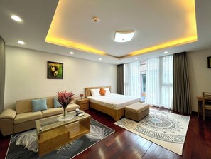 A modern hotel room with a bed, sofa, coffee table, and a large window with curtains.