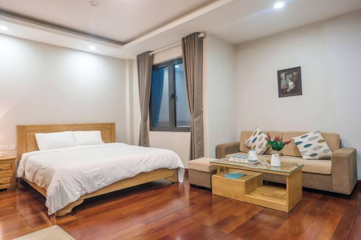 Une chambre à coucher avec un lit, une table de chevet en bois, un canapé, une table basse et une fenêtre avec des rideaux.