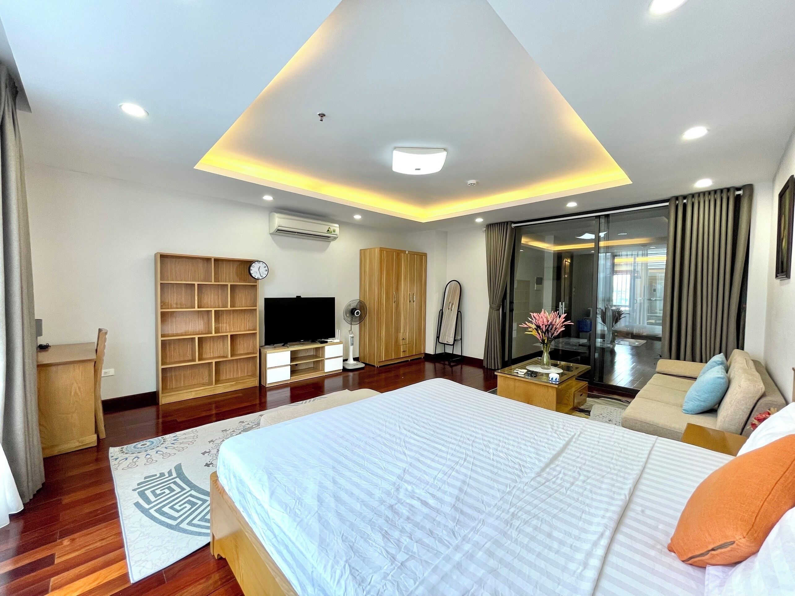 A modern hotel room with a large bed, a TV, a wardrobe, a desk, and a sliding glass door to the balcony.