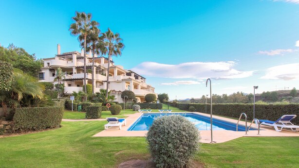 Un edificio residencial con piscina, rodeado de céspedes cuidados y palmeras.