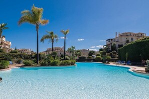 Une piscine entourée de palmiers et d’immeubles.