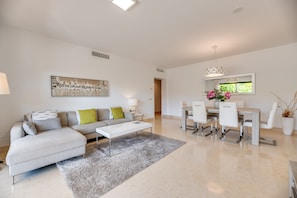 Un salon moderne comprenant un canapé, une table basse, une table à manger avec des chaises, un tableau et une fenêtre donnant sur un beau paysage.
