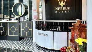 Ein Hotel-Rezeptionsbereich mit modernem Design, mit einem Kronleuchter, einem Empfangsschalter und einer Wand mit dekorativen Elementen, auf der der Hotelname zu sehen ist.