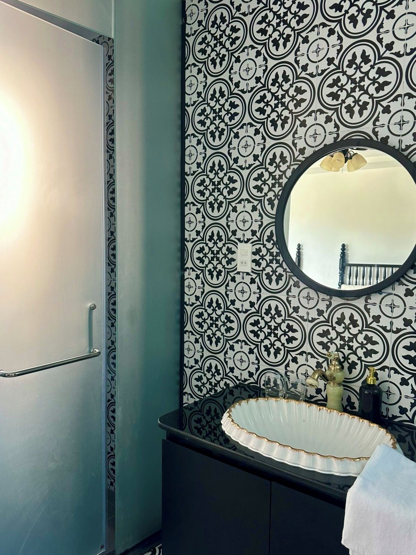 A bathroom with a patterned wall, a round mirror, a sink with a decorative basin, and a towel hanging on the wall.
