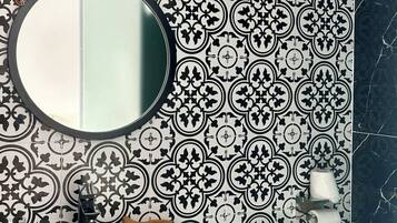 A bathroom with a white sink, a round mirror, a toilet, and patterned tiles.
