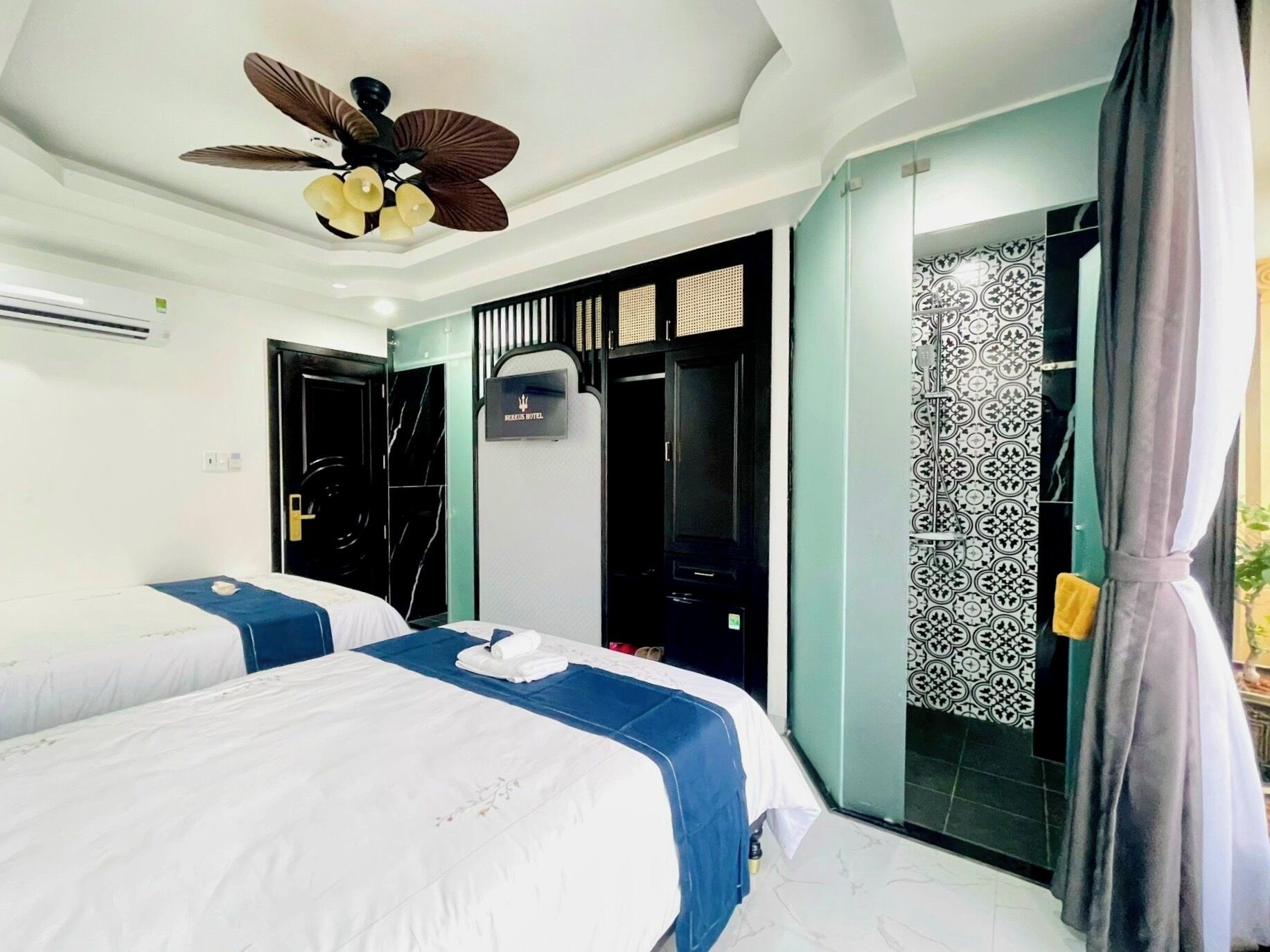 Ein Hotelzimmer mit zwei Betten, einem Deckenventilator, einer Minibar und einem strukturierter Duschbereich.