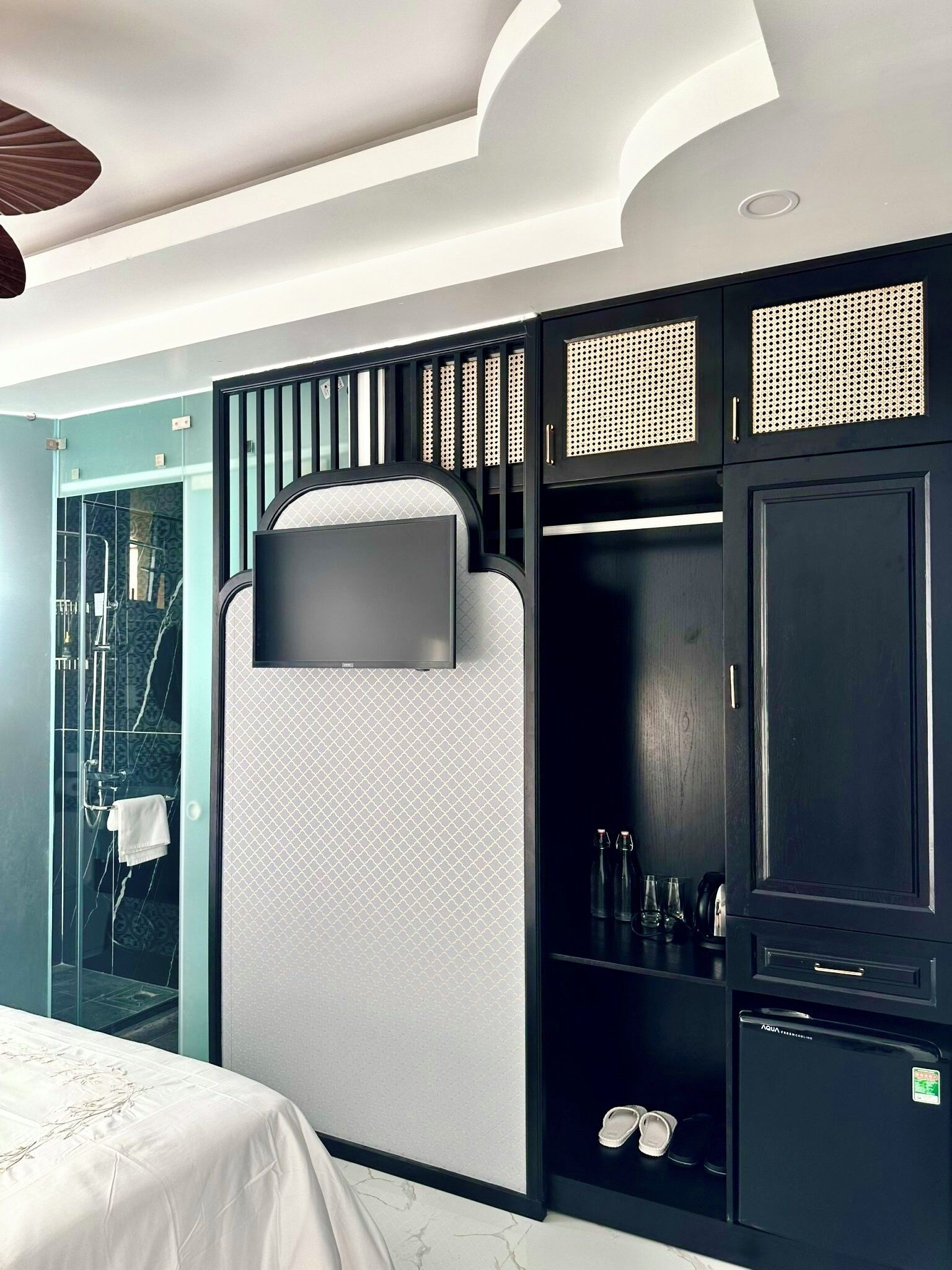A modern hotel room with a bed, a built-in TV, a wardrobe, and a small refrigerator.