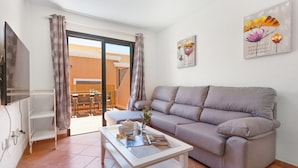 Una sala de estar con sofá, mesa de centro, televisor y puerta corredera de cristal que da a un balcón.