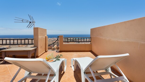 Una terraza con dos sillones blancos, una mesa y una antena de televisión.