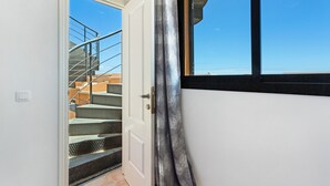 Una puerta que da a una escalera con barandilla de metal, una ventana con marco negro y un cielo azul claro visible a través de la ventana.