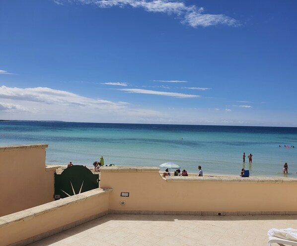 Terraza en la azotea con vistas al mar, algunas personas y un paraguas verde.