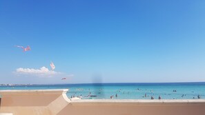 Una playa con cielos despejados, una orilla arenosa y gente nadando en el agua.