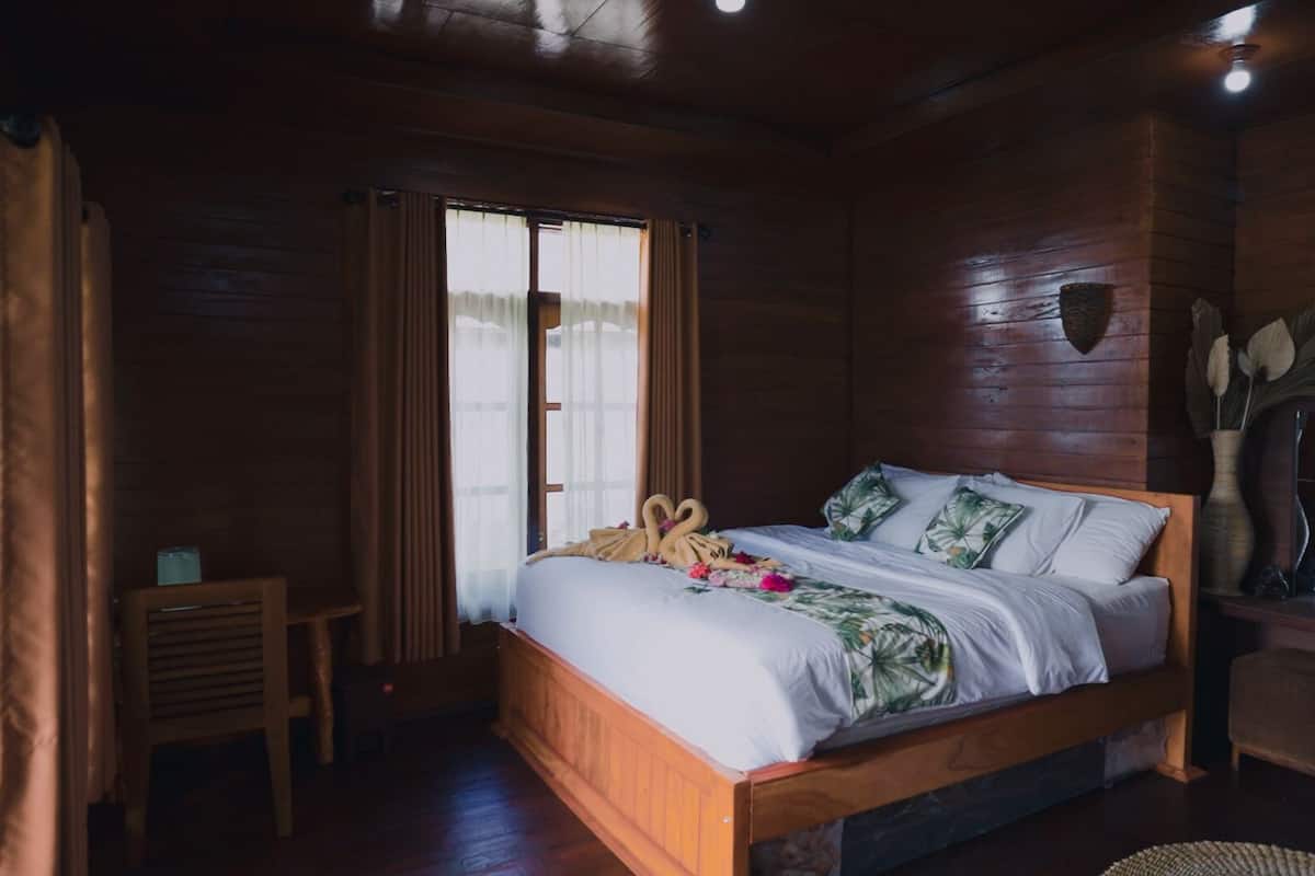 Un dormitorio tipo cabaña de madera con una cama, una mesita y una ventana con cortinas.