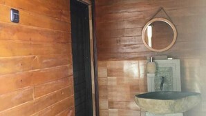 Un baño con paredes y puerta de madera, un lavabo con espejo y un cubo de basura.