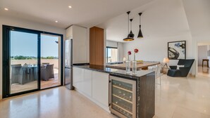 Une cuisine moderne dotée d’un réfrigérateur à vin, de grandes fenêtres et d’un coin repas avec une table et des chaises.