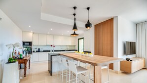 Une cuisine moderne avec des meubles blancs, une table à manger en bois et des luminaires suspendus.