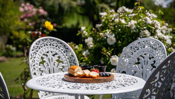 A round table with a white metal chair, a wooden board with bread and berries, and a small bowl of strawberries.