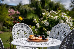 A round table with a white metal chair, a wooden board with bread and berries, and a small bowl of strawberries. - Classic Bach with Wifi  and pets (Taupō)