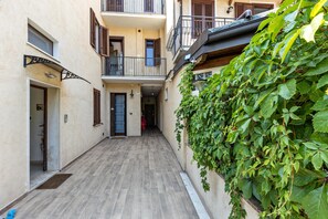 Un stretto vicolo con pavimento in legno, una porta a sinistra e un muro ricoperto di piante rampicanti.