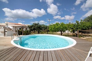 A wooden deck with a circular swimming pool, a white fence, and a building with a red-tiled roof in the background. - Holiday Apartment 'Casa Do Livramento Adega' with Shared Pool, Wi-Fi and Air Conditioning (Tavira)